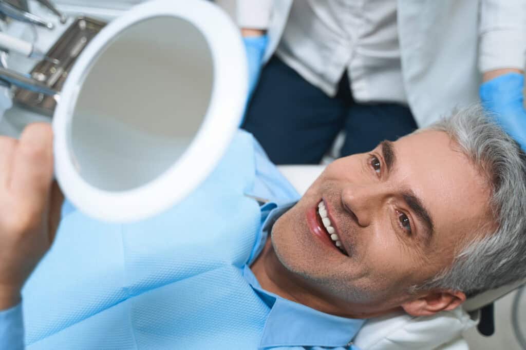 Patient smiling after his dental implants while seeing the mirror