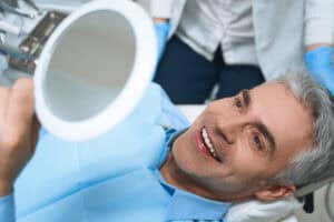 Patient smiling after his dental implants while seeing the mirror