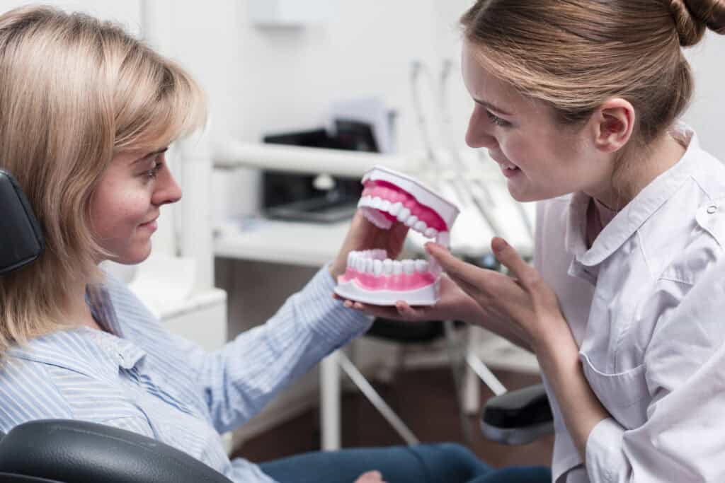 A dentist shows a dental model to a patient in a dental chair.